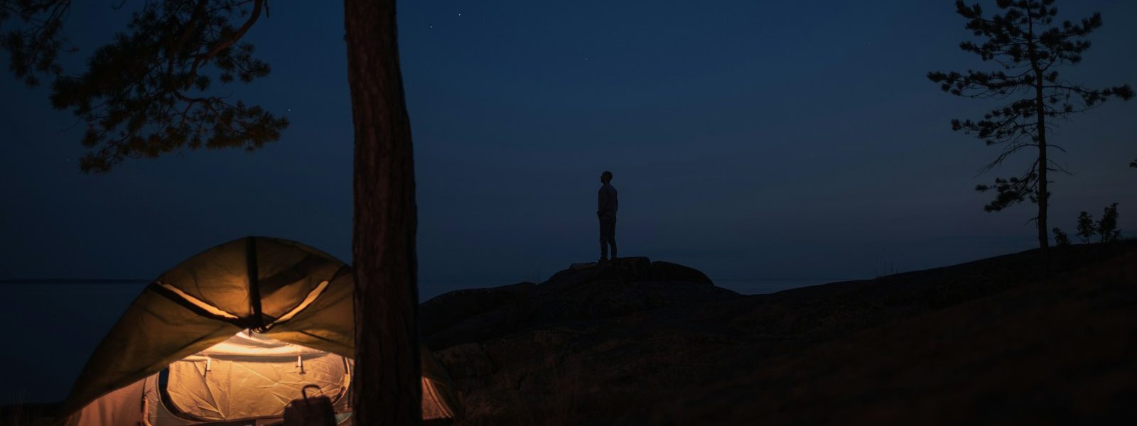 silhouette of person standing on rock near tent during night time
